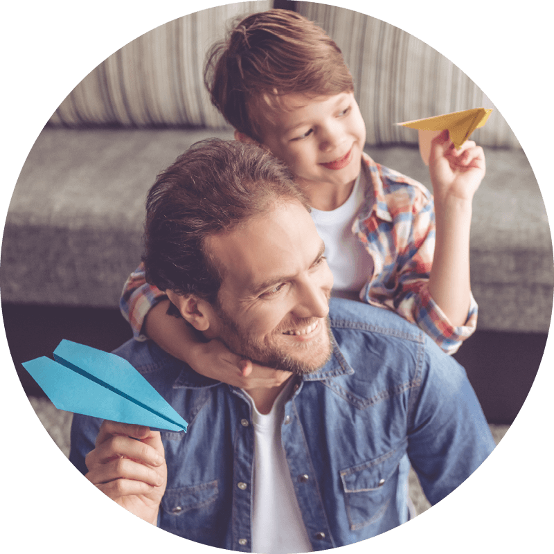 An Eversense CGM user holds a blue paper airplane while smiling, with a child on his back holding a yellow one.